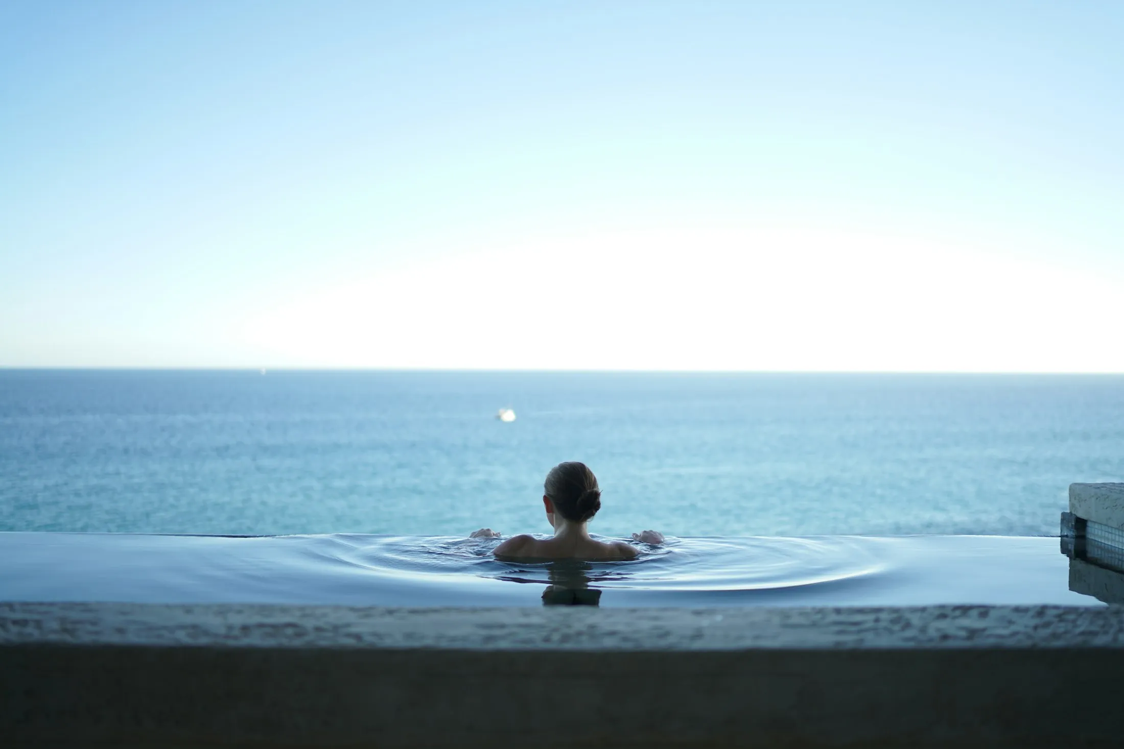 A woman relaxing in an infinity pool facing a blue ocean horizon