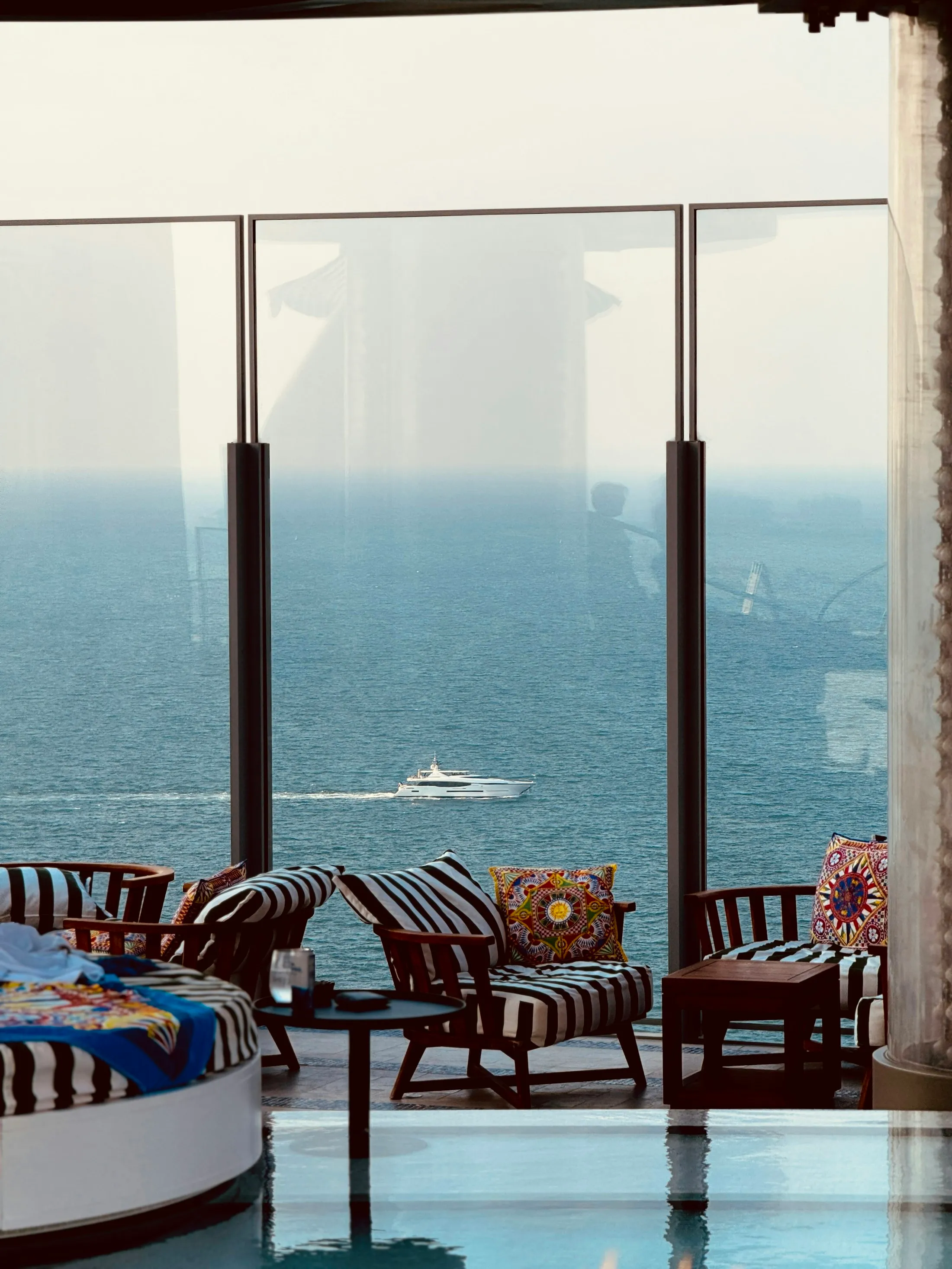 Striped lounge chairs inside a Dubai suite overlooking the sea and a passing boat