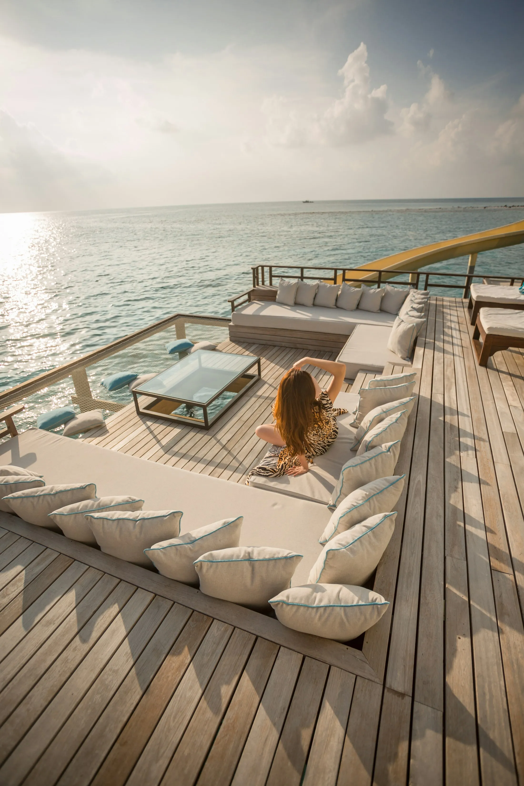 A sunlit Maldives overwater deck with cushioned seating above the sea
