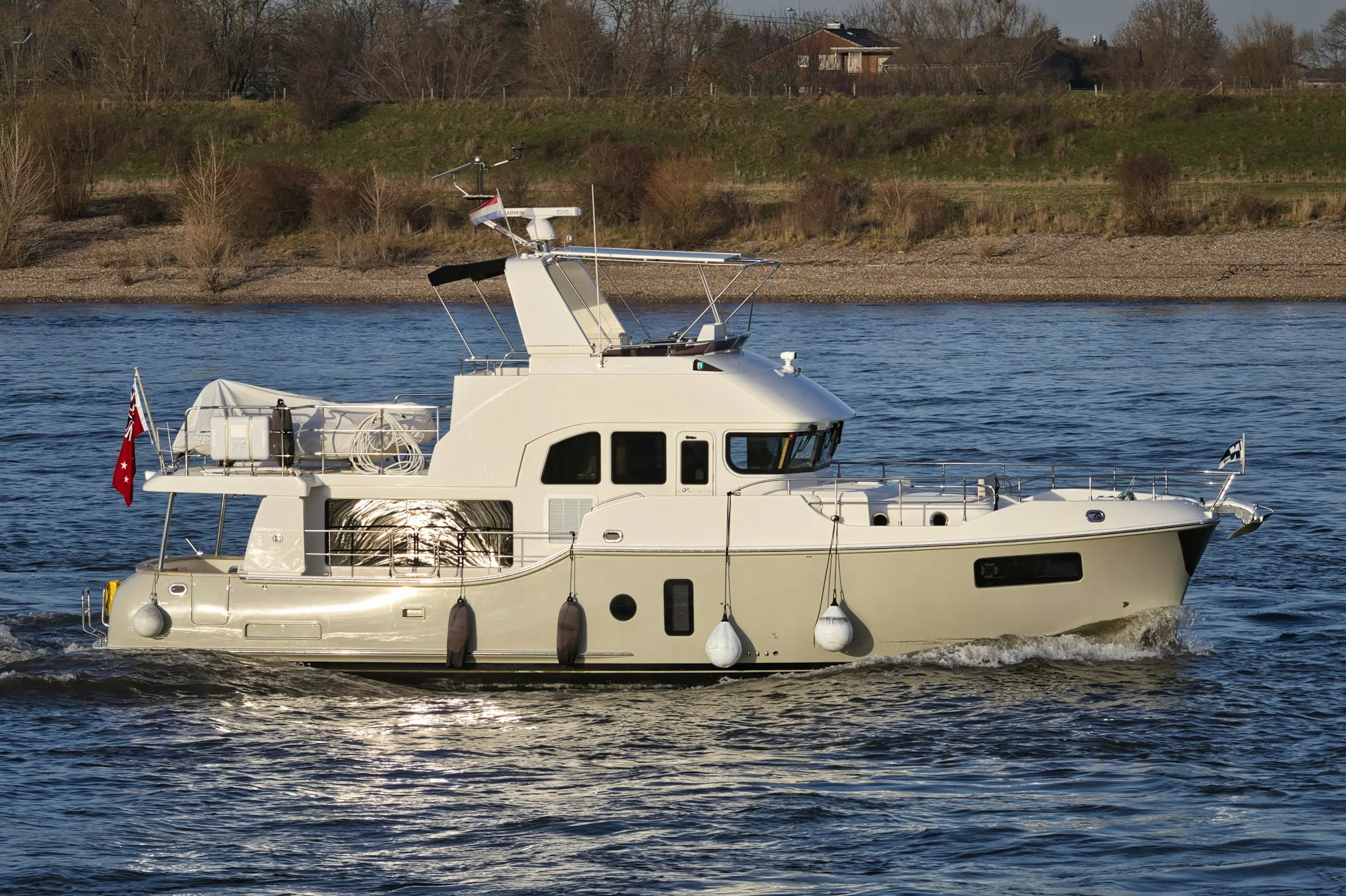A modern yacht sailing along a wide river in afternoon light