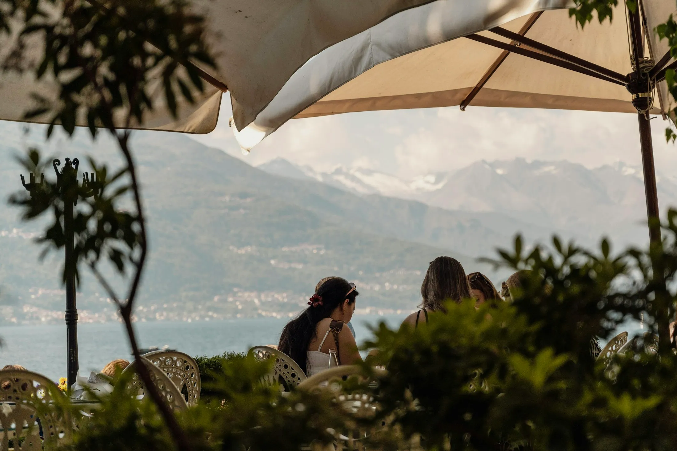 Diners seated under an umbrella beside Lake Como with mountains in the distance