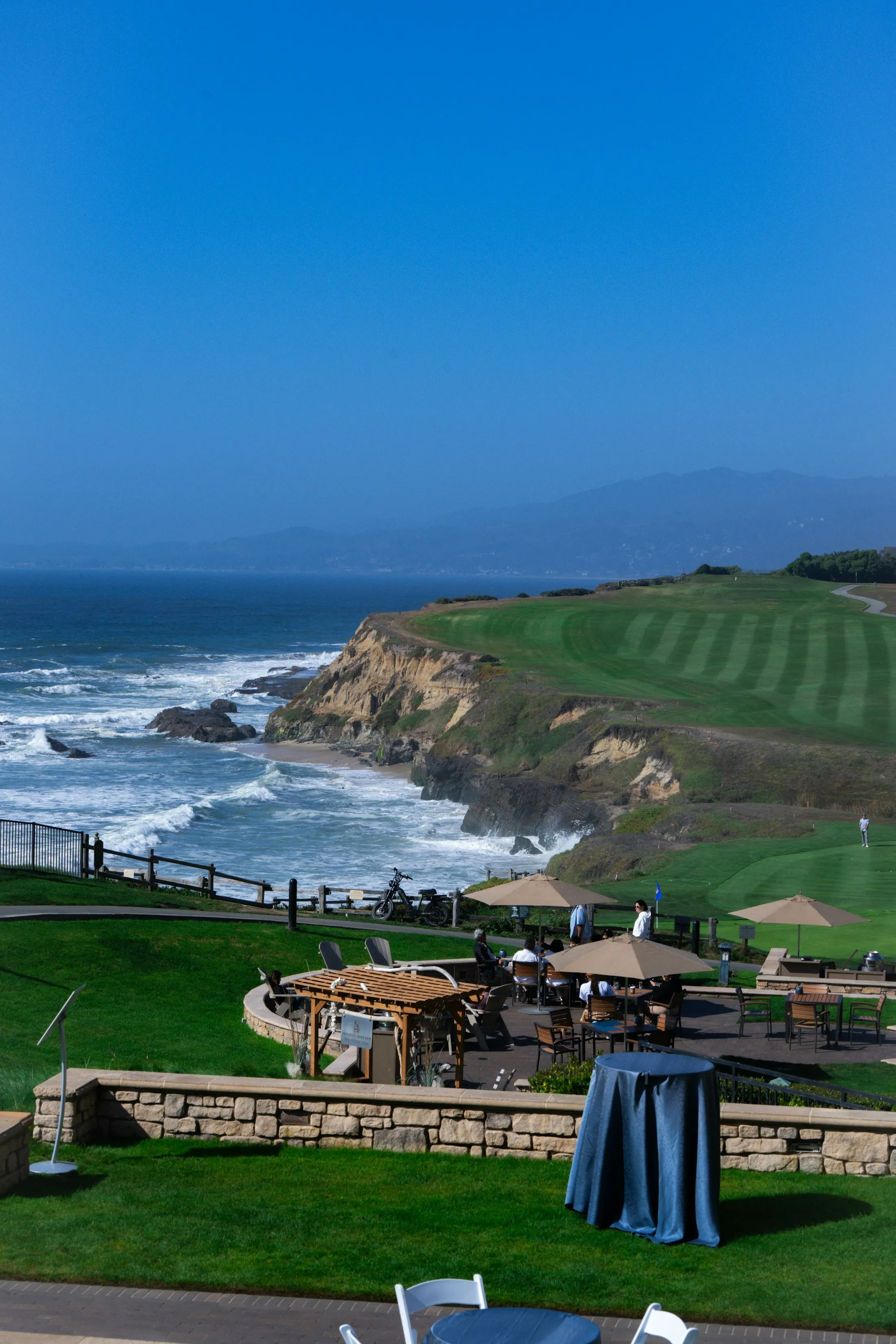 A coastal golf course with dining tables overlooking the ocean and cliffs
