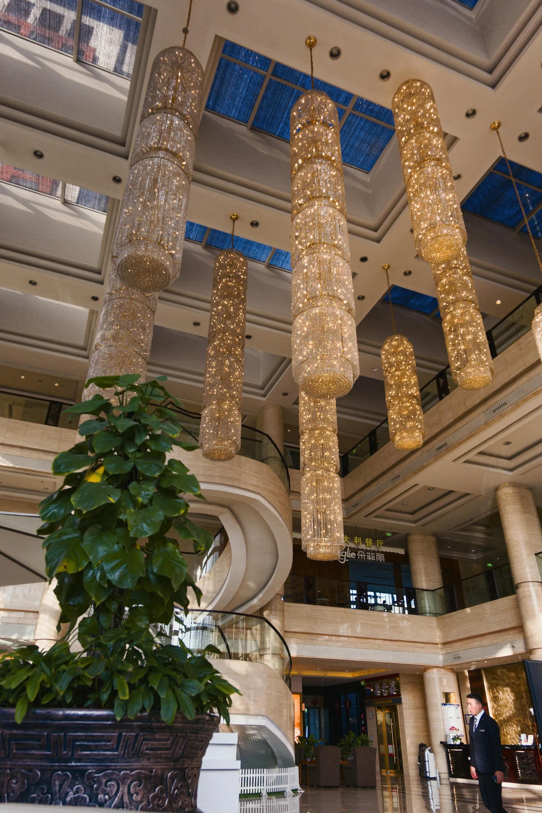 A grand hotel lobby with ornate lights, plants, and guests moving through