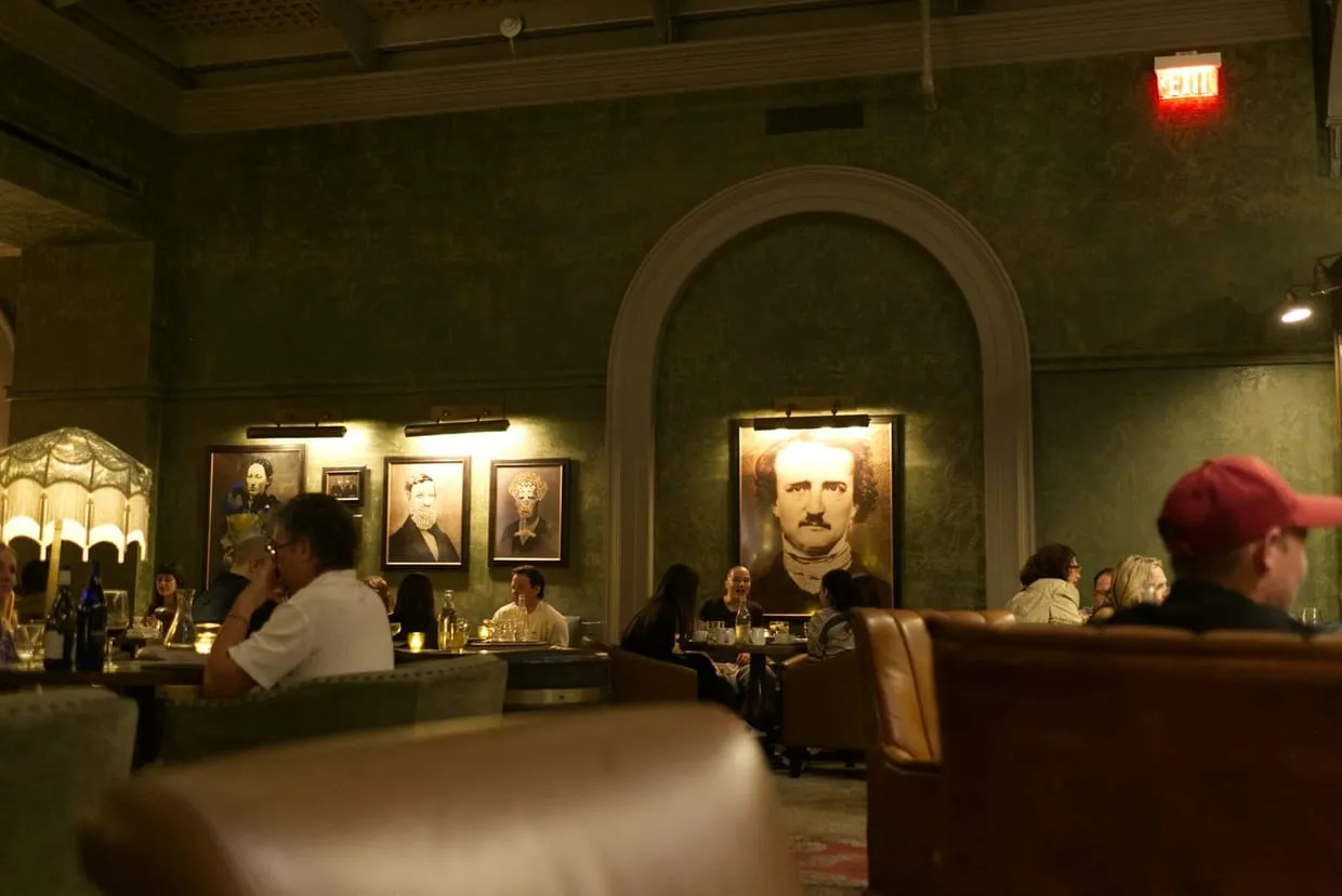 A dim green dining room with framed portraits, low lamps, and well-spaced leather banquettes